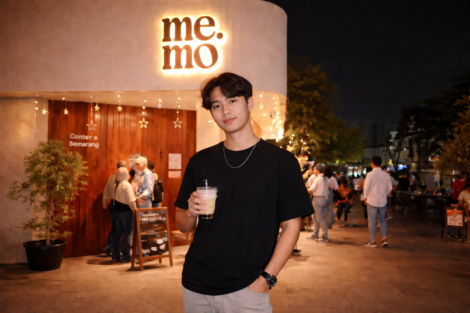 Pria memakai kaos hitam berdiri di depan Memo Coffee Semarang pada malam hari dengan lampu hangat dan suasana kafe yang ramai
