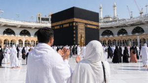 Pasangan jamaah umroh berdoa menghadap Ka'bah di Masjidil Haram dengan suasana ramai dan penuh kekhusyukan