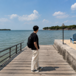 Pria sedang menikmati pemandangan laut di dermaga pantai dengan suasana cerah dan tenang